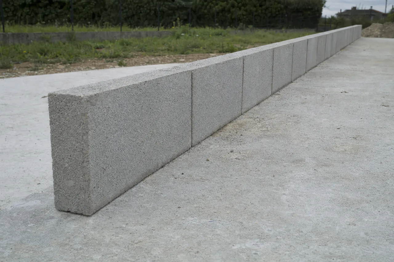 A single straight course of plain grey concrete blocks laid dry on a concrete slab seen from a low angle — block wall, Bowling Green. Illustrative example.